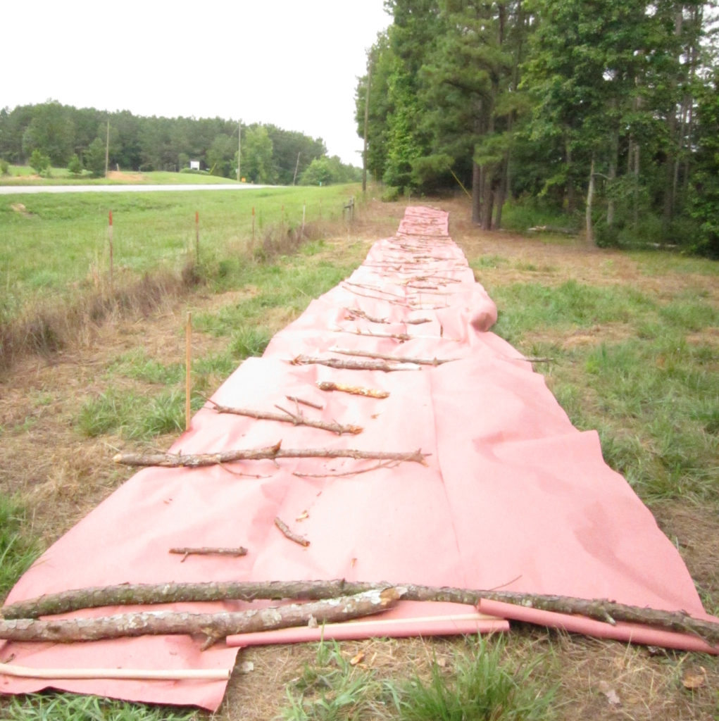 long strip of pink fabric laid on top of grass in a field at the farm