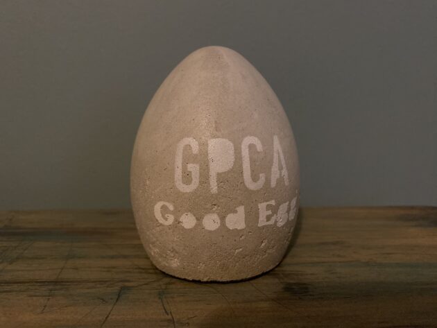 A gray egg-shaped “Good Egg” Award, with white writing on the front that says "GPCA Good Egg."